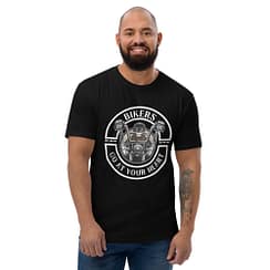 A bearded man smiles, wearing a Looga Black T-Shirt for Bikers - Comfort Meets Style, featuring motorcycle handlebars, a skull, and the phrase Bikers Go At Your Heart, showcasing his passion for the road. His tattooed right arm adds to his adventurous allure.