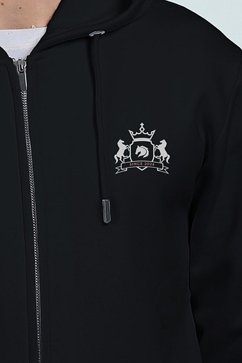 A person wears a thick, embroidered black hoodie with a silver emblem on the chest featuring two horses, a shield, and a crown beneath SINCE 2013. The hoodie includes a zipper and drawstrings.